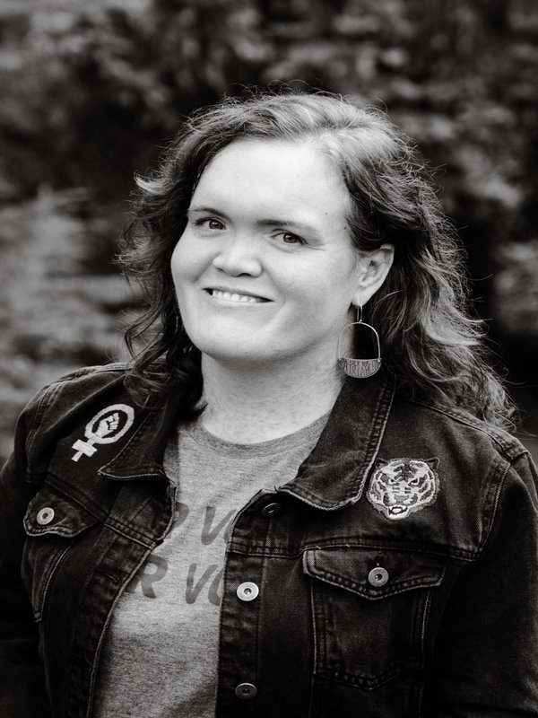 Professional headshot of Carrie Griffin Basas, Esq. - a warm, approachable photo showing her in a denim jacket with pins, representing her authentic and fierce personality